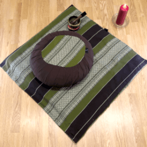 Meditation cushion, singing bowl and candle on wooden flooring